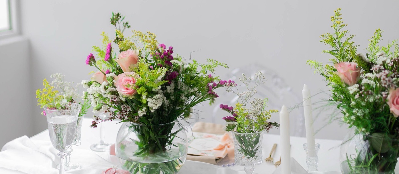 Mesa de festa clara, com arranjos de flores, velas e taças